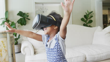una chica afroamericana sonriente jugando con auriculares vr en la sala de estar