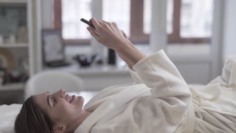 Mujer-Sonriendo-Y-Enviando-Mensajes-De-Texto-En-Su-Teléfono-Mientras-Está-Acostada-En-La-Mesa-En-Un-Spa