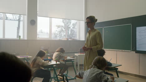 teacher walking between desks with students. pupils writing in notebooks