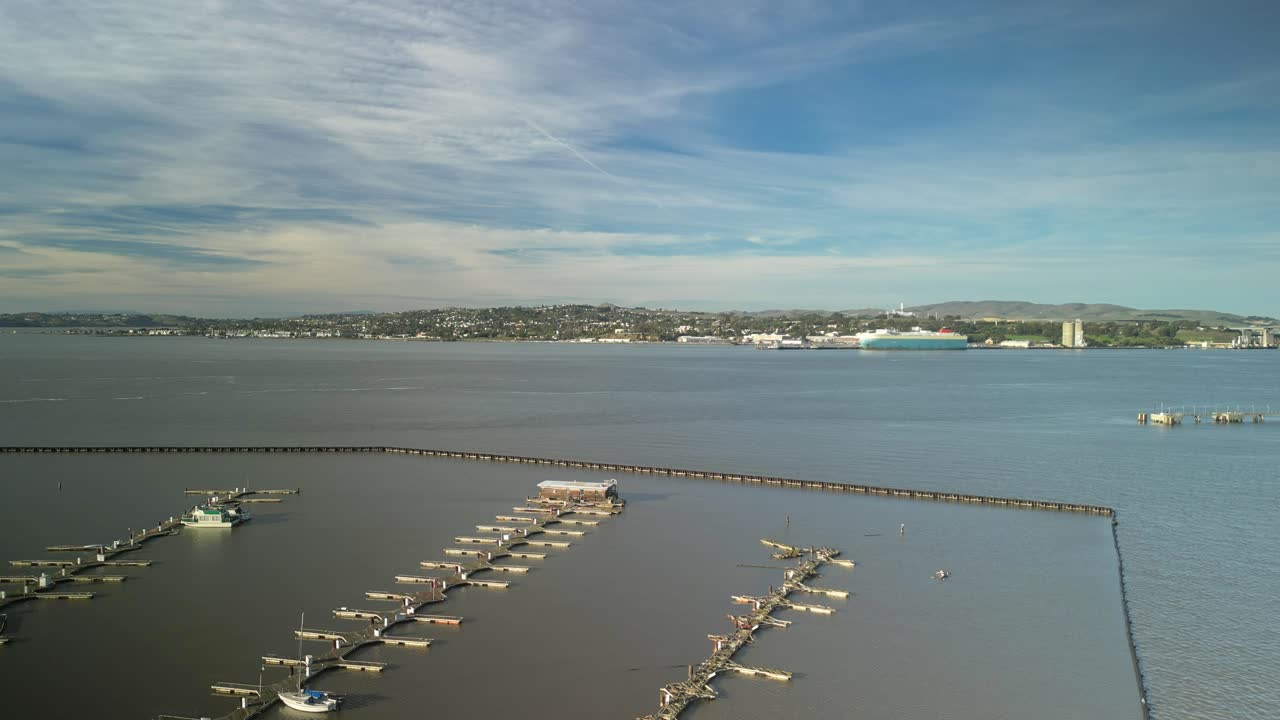 Aerial ascend over empty dock piers of Carquinez Strait wetlands and shoreline in Martinez, California, with hills on horizon