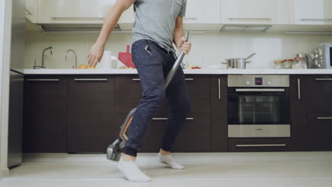 Closeup-man-legs-cleaning-floor-with-vacuum-cleaner-at-kitchen.