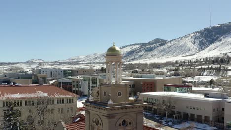 An-aerial-drone-shot-moving-backwards-from-a-small-tower-in-the-middle-of-a-small-town-overlooking-snowy-mountains-in-the-winter