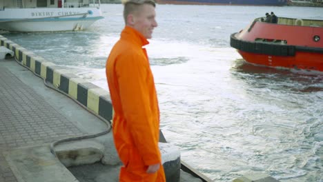 young port worker in orange uniform waving his hand to the ship that is riding and going away