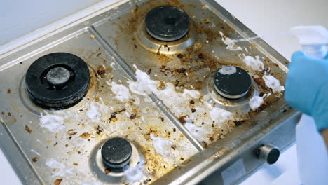 cleaning a greasy kitchen stove surface. a person cleans a dirty stove with grime and stains using a spray cleaner and cloth in a kitchen setting