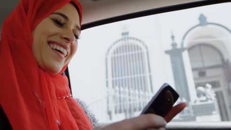 animation of laughing asian woman in hijab with smartphone over cityscape