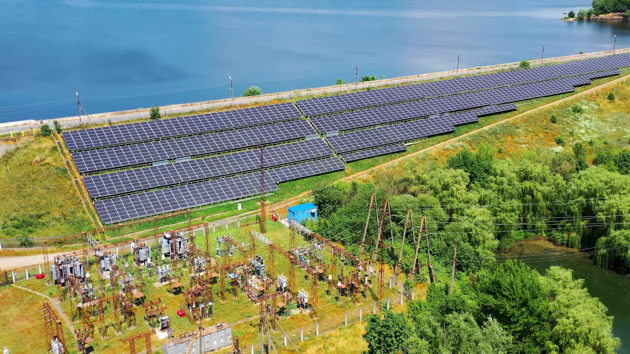 Solar power station in sunny day. Photovoltaic solar panels on blue water background. Electricity station on the bank of a river. View from above.