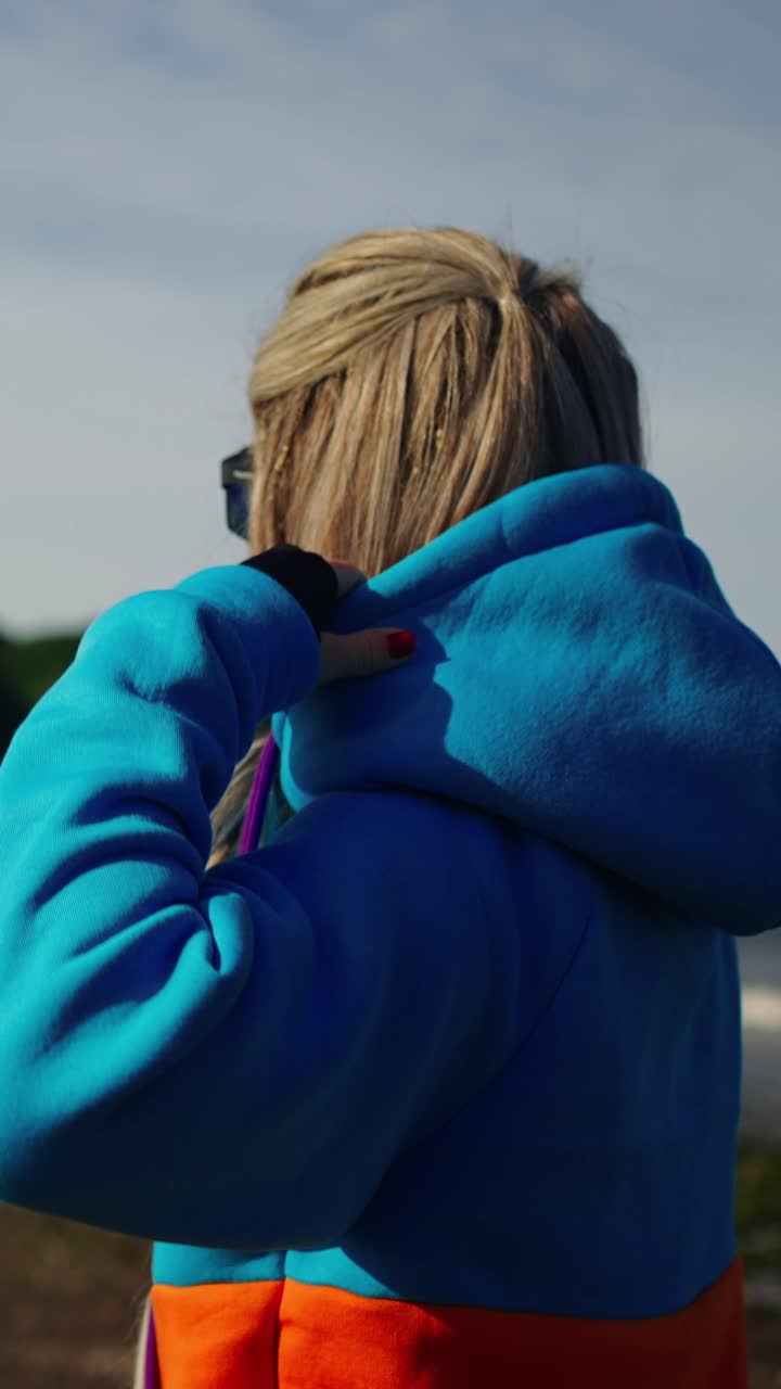 Woman Adjusting Hoodie and Looking at Scenic Coastline