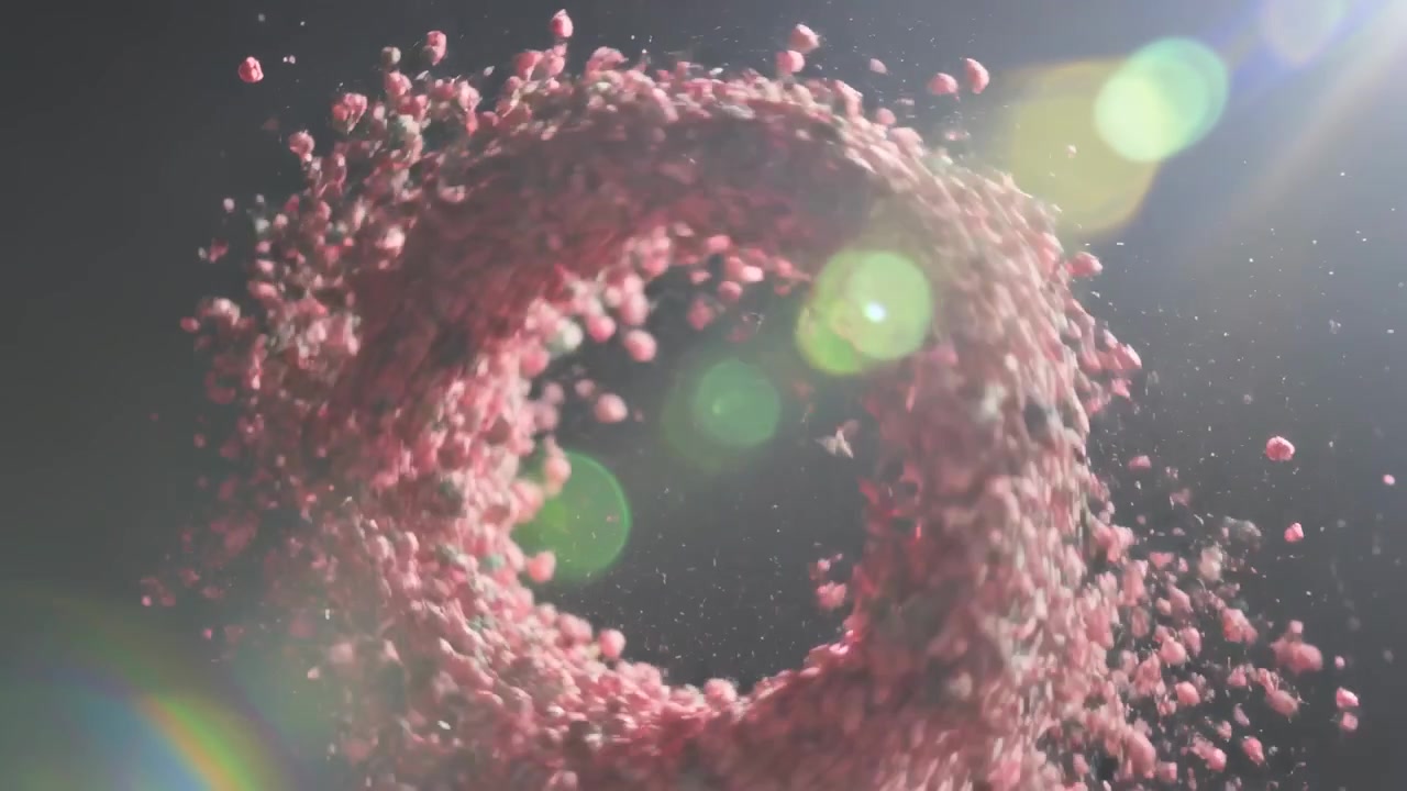 오른쪽 상단의 녹색 플레어 아래, 스튜디오에서 바깥쪽으로 조각들을 흩뿌리며 회전하는 분홍색 알갱이 토러스.