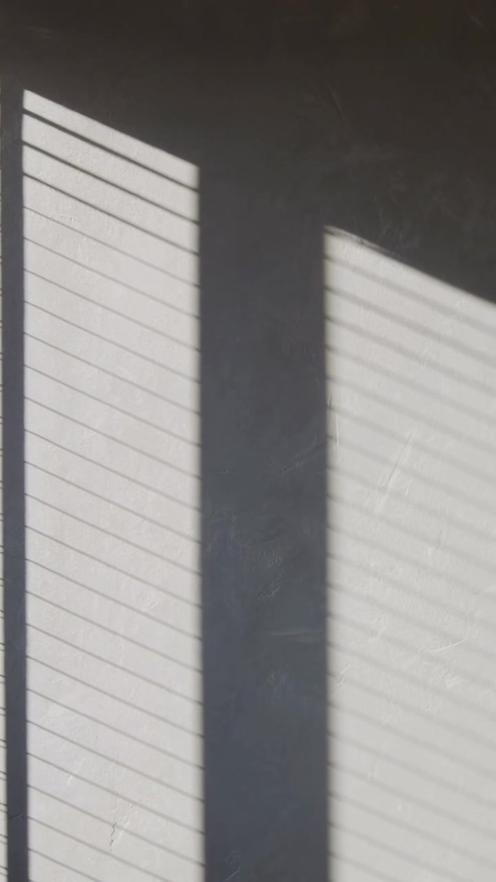 Vertical video: Casting light through window blinds forming slanted shadows on mullion wall at home