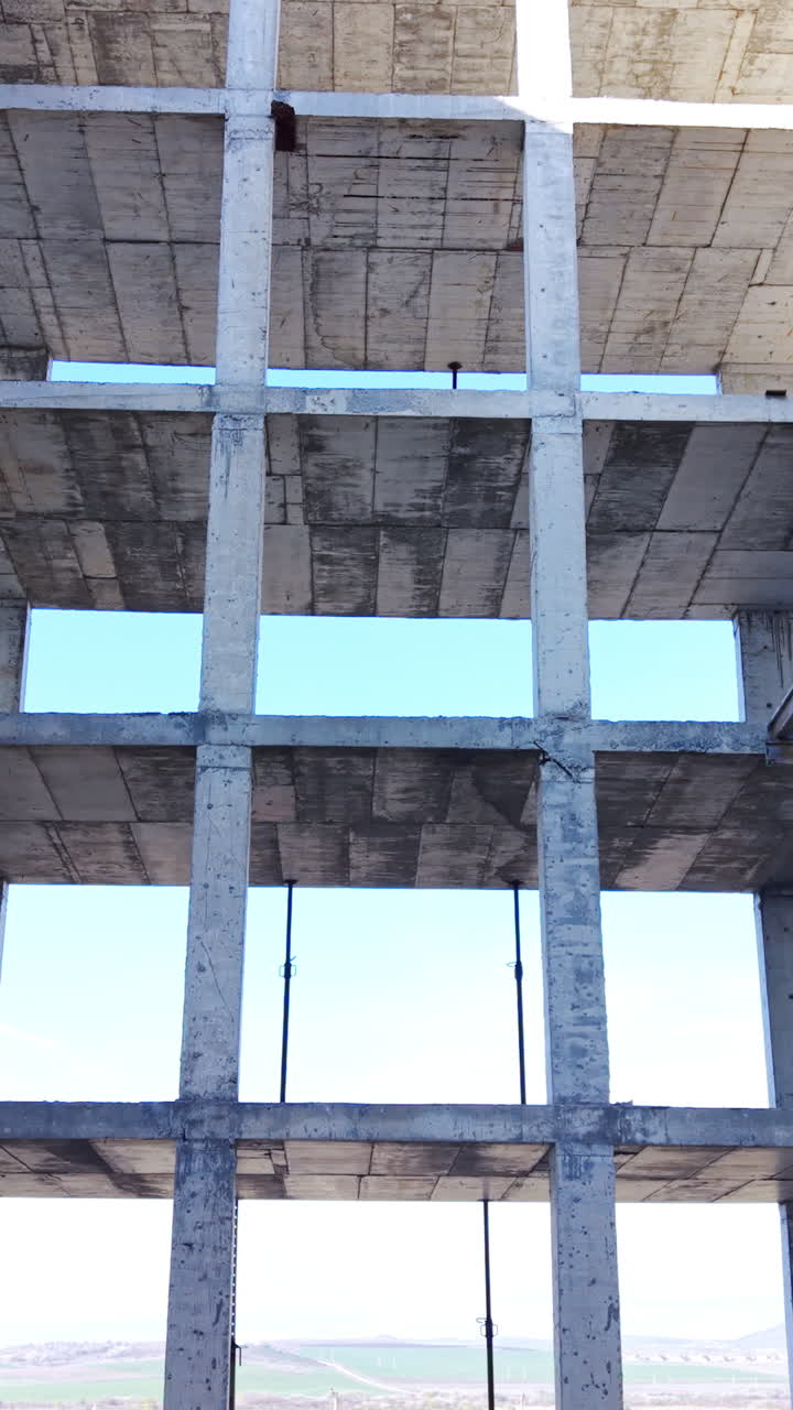 Struttura in cemento armato con supporti metallici temporanei e sfondo di cielo blu. Scheletro in cemento di un edificio incompiuto con pilastri di supporto. Video verticale