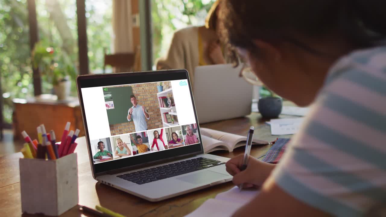Schoolgirl using laptop for online lesson at home, with diverse teacher and class on screen