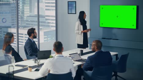 diverse office conference room meeting: asian female project manager uses green screen chroma key wall tv to present digital investment opportunity for happy investment team. static wide shot