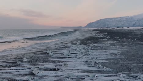 aerial landscape view of ocean waves crashing on to diamond beach, covered in snow, at dusk
