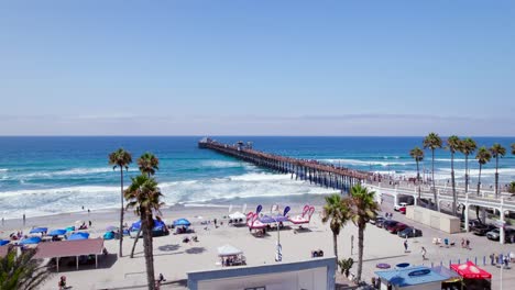 drone elevándose sobre el muelle de oceanside con mucha gente en la playa en verano