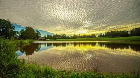 luz del sol dorada y paisaje de nubes reflejado sobre la superficie de agua tranquila de un lago durante el amanecer