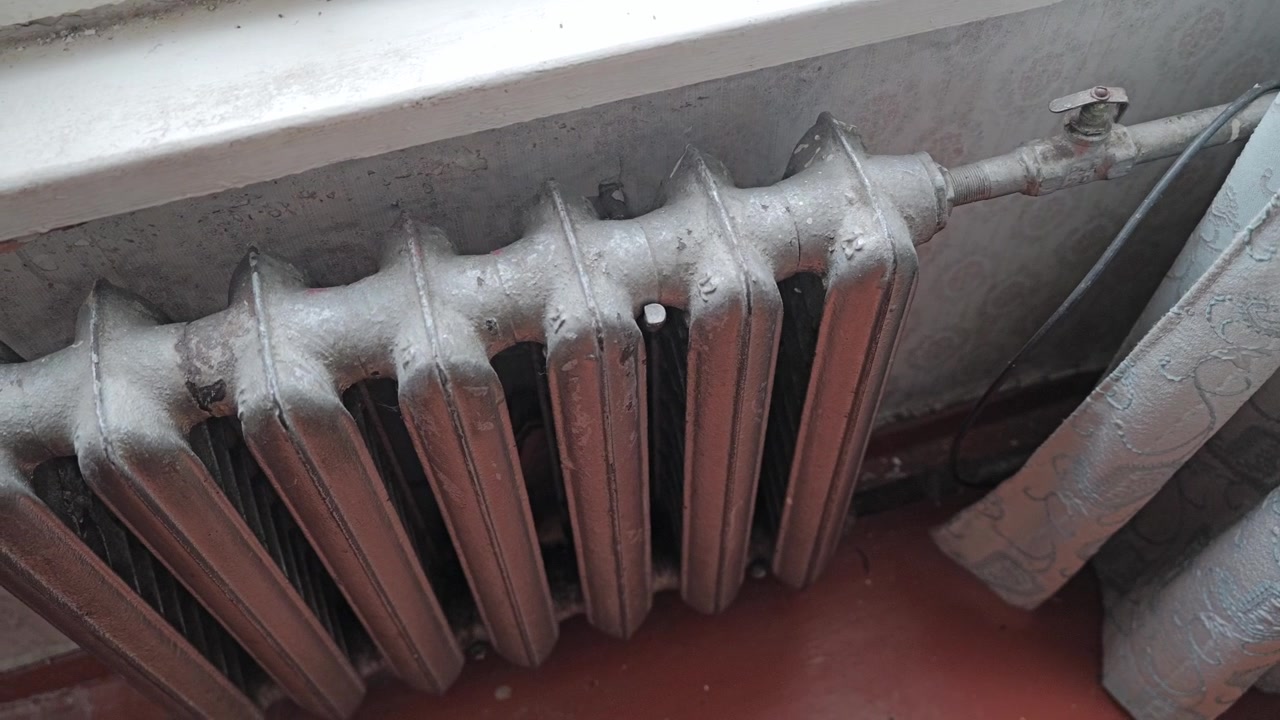 Radiatore in ghisa invecchiato sotto una finestra che evidenzia il design classico del riscaldamento interno