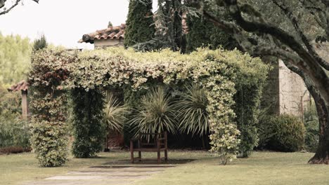 Wooden-bench-under-lush-garden-arbor-surrounded-by-greenery-and-trees