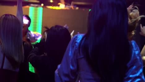 group of people dance in disco night club to the beat of music from dj on stage