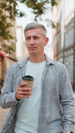 happy mature caucasian man enjoying drinking morning coffee hot drink and smiling on city street