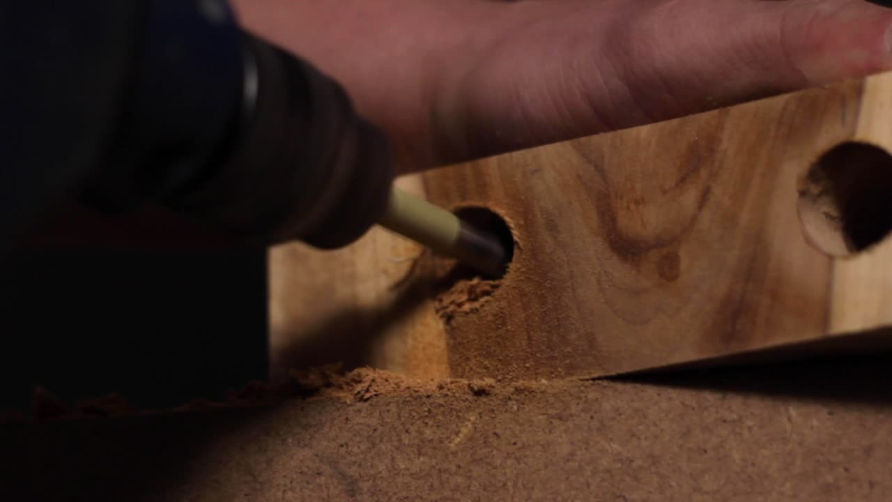 Close up of a carpenter using an electric drill to drill a hole into a slab of wood before retracting the tool, spraying sawdust everywhere