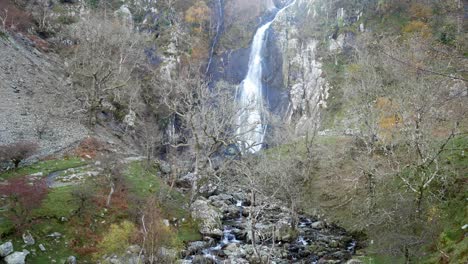 Autumn-nature-trail-leading-to-cascading-waterfall-and-river-through-bare-leafless-trees