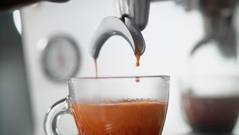 espresso pouring to a steamy transparent cup from a coffee maker's portafilter in slow motion