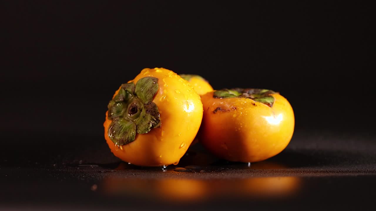 agua goteando sobre los persimiones contra un fondo oscuro