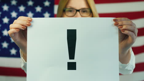 a woman holds a poster with a exclamation mark against the background of the american flag