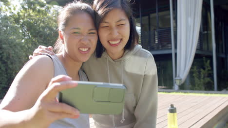 happy asian female friends with water bottle doing selfie and making faces on terrace, slow motion