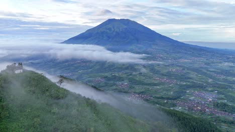 Aerial view from the top of a mountain covered in thin mist shows another mountain. Scenery Mount Merbabu from the peak of Mt Telomoyo