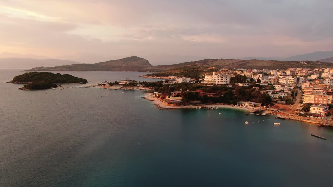 Drone view in Albania flying over blue crystal clear water on sunset, green small islands and hotels in Ksamil