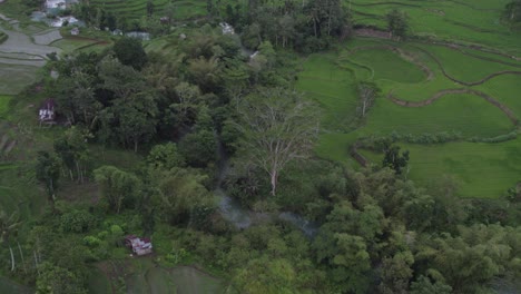 Reveal-shot-of-lush-green-landscape-with-waterfall-at-Sumba-island-Indonesia,-aerial