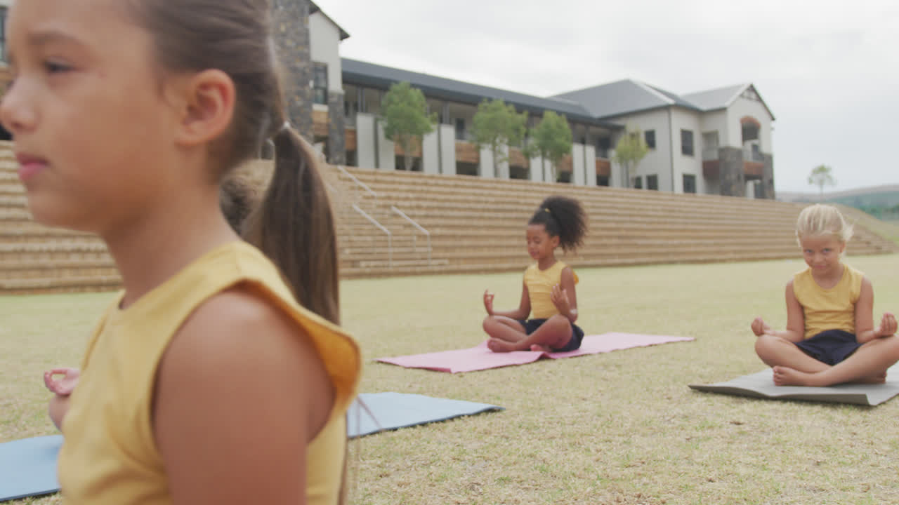 video de niñas diversas enfocadas practicando yoga en esteras frente a la escuela
