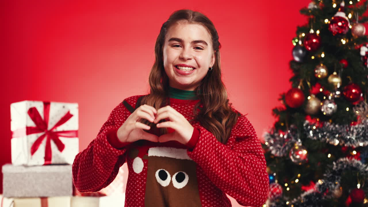 Woman with Christmas Sweater Making Heart Shape in Front of Christmas Tree