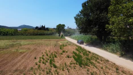 Drohnenaufnahme-Eines-Blauen-Autos,-Das-Bei-Sonnigem-Wetter-In-Einer-Spanischen-Gegend-Fährt