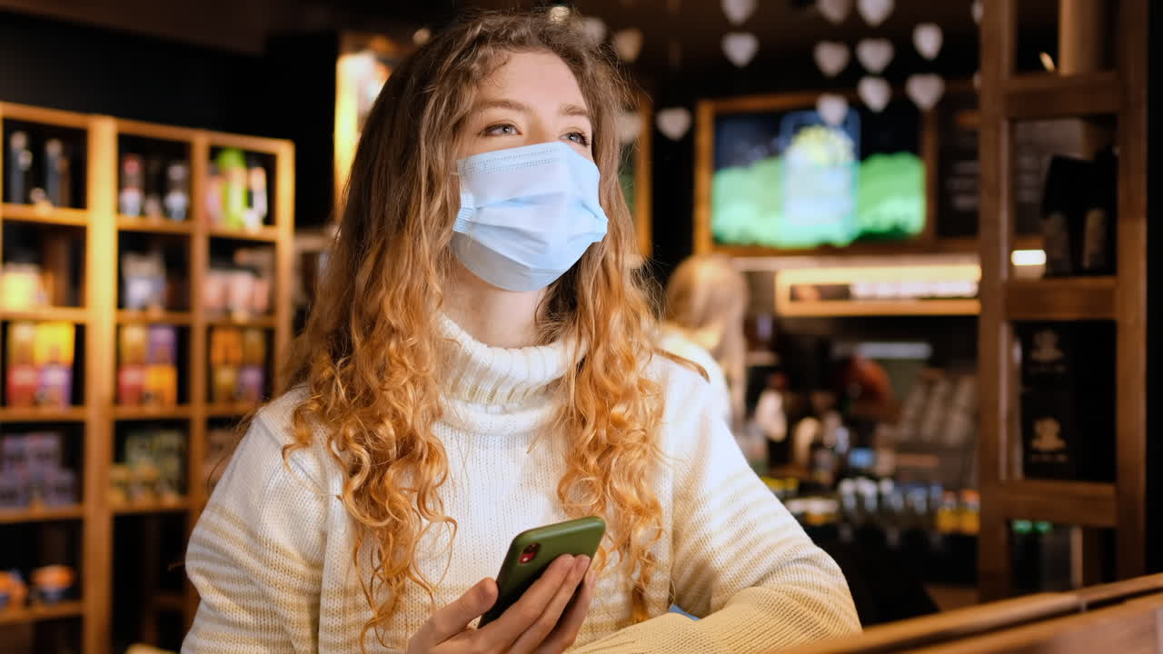 Donna con mascherina medica che mostra a un barista in un bar uno smartphone con il certificato di vaccinazione internazionale COVID-19. Dose di richiamo. Scansione del codice QR. Interni di un bar