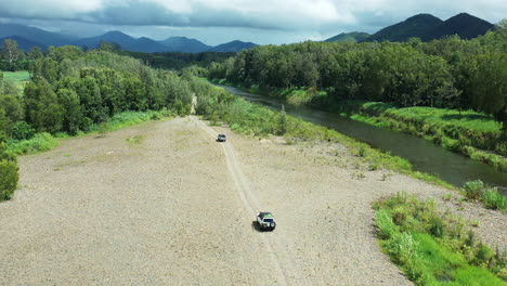 aerial drone over four wheel drives off road on gravel near creek in australian countryside, 4k