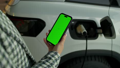 mujer cargando un vehículo eléctrico con un teléfono móvil de pantalla verde
