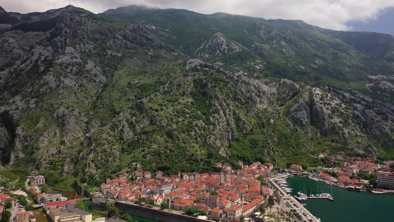 Prachtige drone-opname vanuit vogelperspectief van de historische oude stad Kotor, Montenegro. Met traditionele rood-pannendaken, een kristalheldere riviergracht, een kustjachthaven en steile kalkstenen bergen