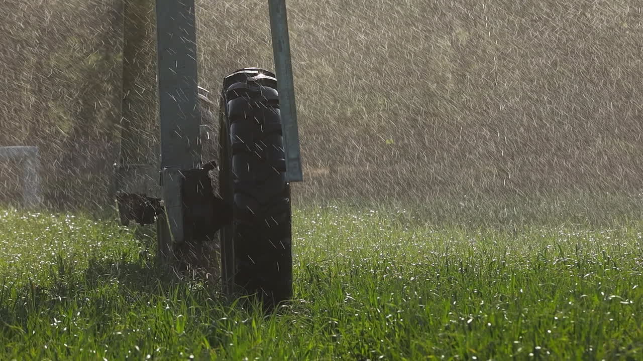 Hjul fra centerpivot-vandingsanlæg på vådt græs med baggrundsbelyst vandtåge