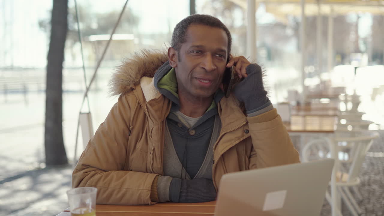 hombre de mediana edad sonriendo hablando por teléfono celular en una cafetería