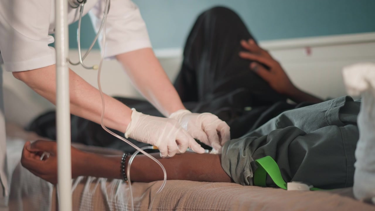Mann erhält zu Hause eine intravenöse Behandlung. Eine Person liegt während der IV-Therapie unter engmaschiger Aufsicht. Der Patient liegt flach und wird während der intravenösen Infusion in seiner Wohnung sorgfältig überwacht.