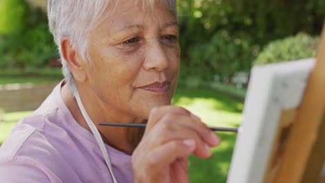 video de una feliz mujer mayor biracial pintando en el jardín