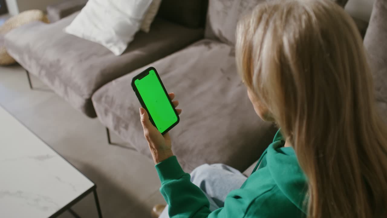 Woman using a phone with green screen in living room