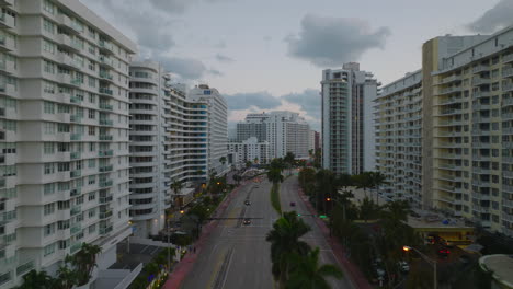 Evening-in-modern-city-borough-with-multilane-trunk-road-lined-by-high-rise-apartment-buildings.-Forwards-fly-at-dusk.-Miami,-USA