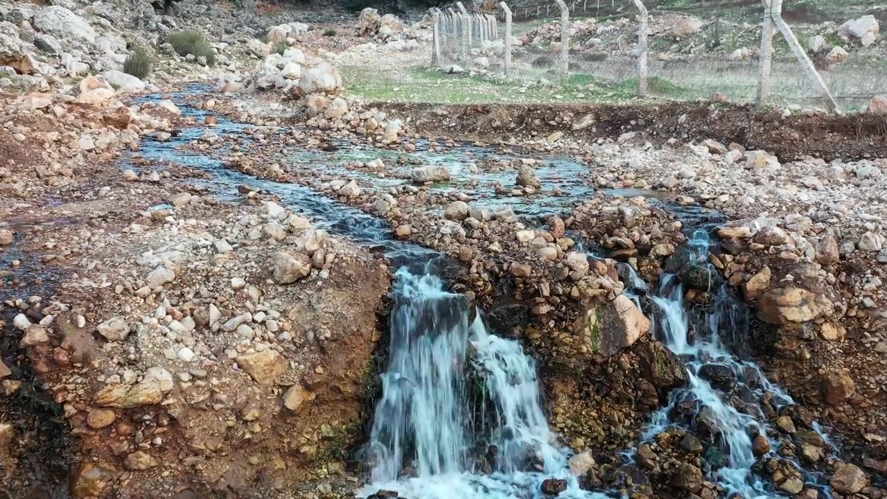 Pequena cachoeira natural fluindo por terreno rochoso em uma paisagem montanhosa marroquina com água cristalina e texturas rústicas. Ideal para projetos de natureza e documentários.