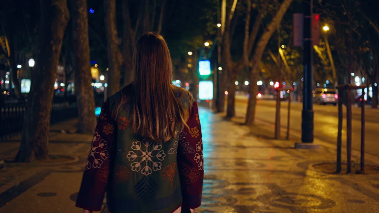 оглядываясь назад, девушка поворачивает к камере поздно вечером. женщина идет по городской улице.