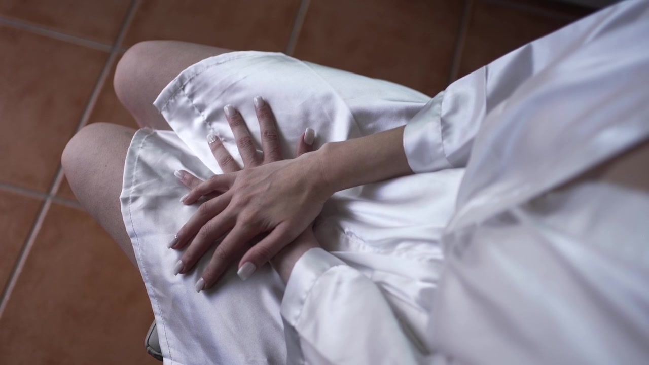 Primo piano delle mani di una donna appoggiate in grembo, che indossa una vestaglia di seta con un anello delicato