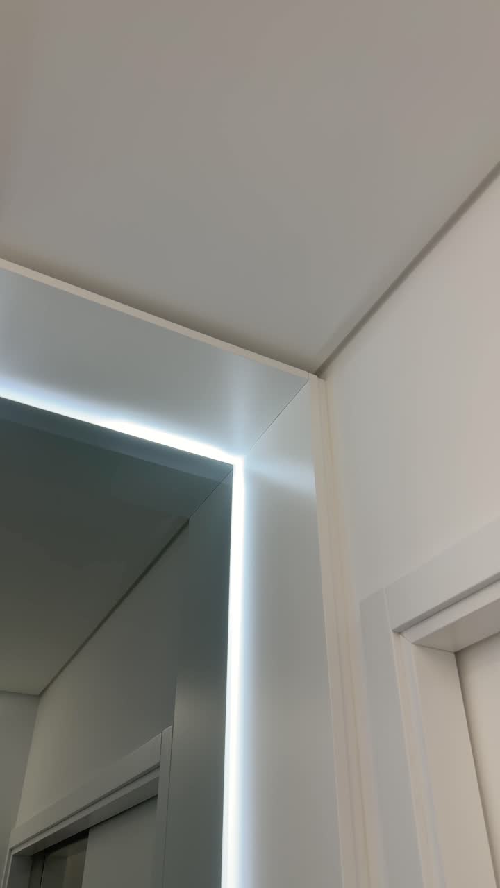 Dettaglio verticale dell'angolo di uno specchio da bagno retroilluminato e della parete bianca del soffitto.