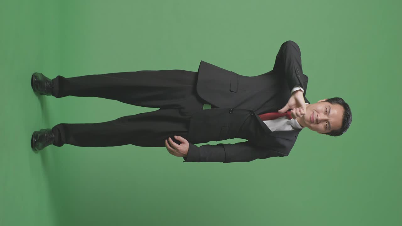 녹색 스크린 스튜디오에 서있는 동안 엄지손가락을 아래로 표시하는 아시아 사업가의 몸으로 가득 차 있습니다.